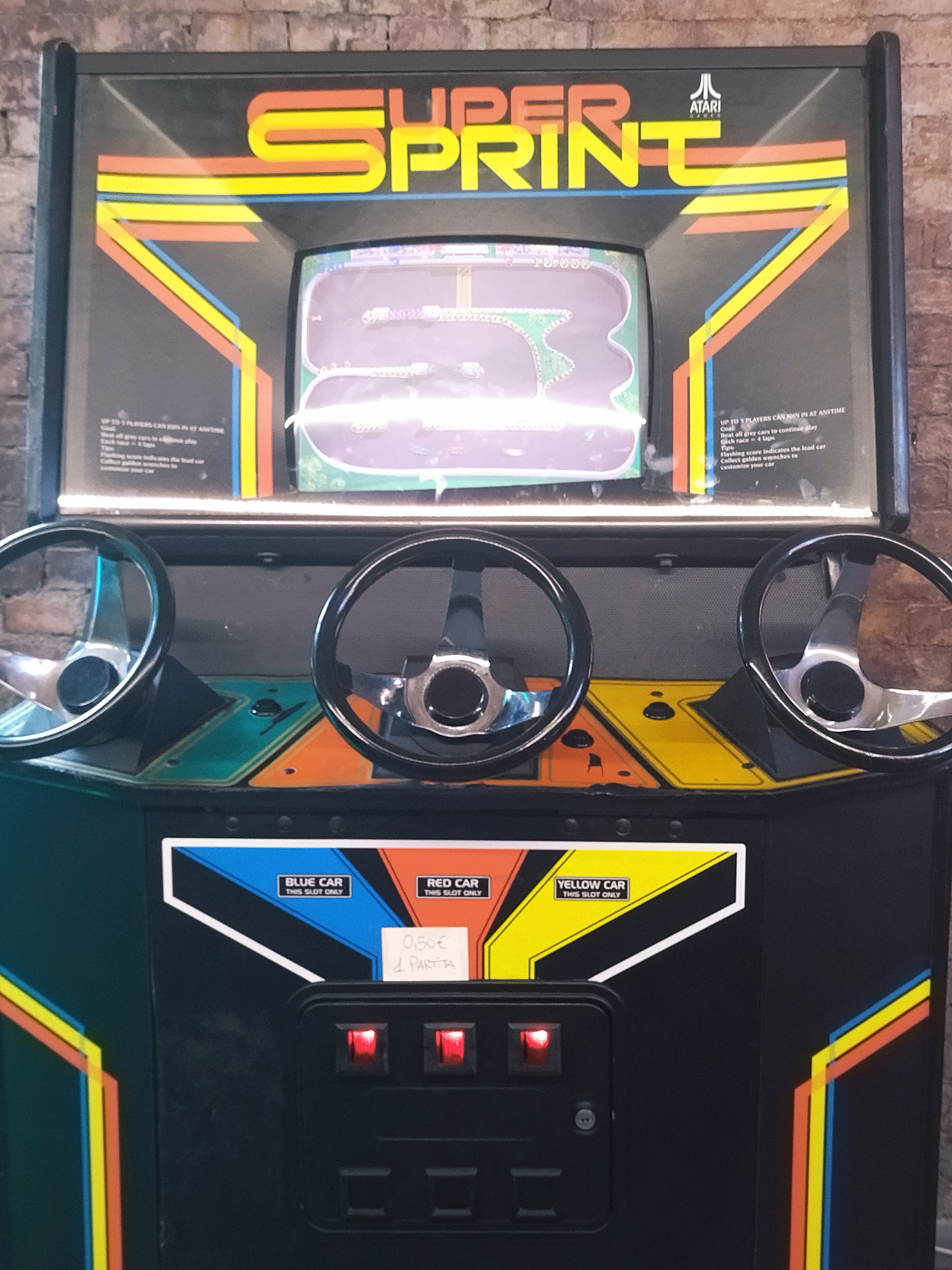 Videogioco retro di corsa Atari Super Sprint, con schermo CRT, tre volanti, all'interno dell'area al chiuso.